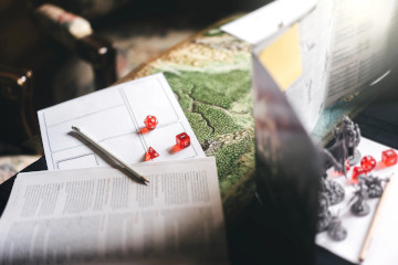Auf einem Tisch steht ein Spielleiterschirm neben Würfeln und Figuren für den Tabletop RPG Game Master.