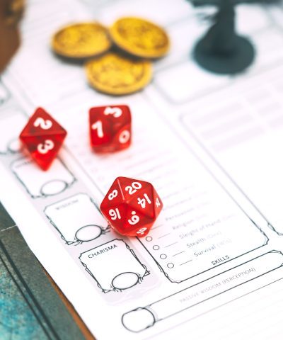Rote Würfel und Goldstücke liegen auf einem Charakterbogen für Rollenspiele.